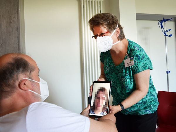 Seelsorgerin hält Tablet für Patienten, der mit Angehörigen per Videoanruf spricht.
